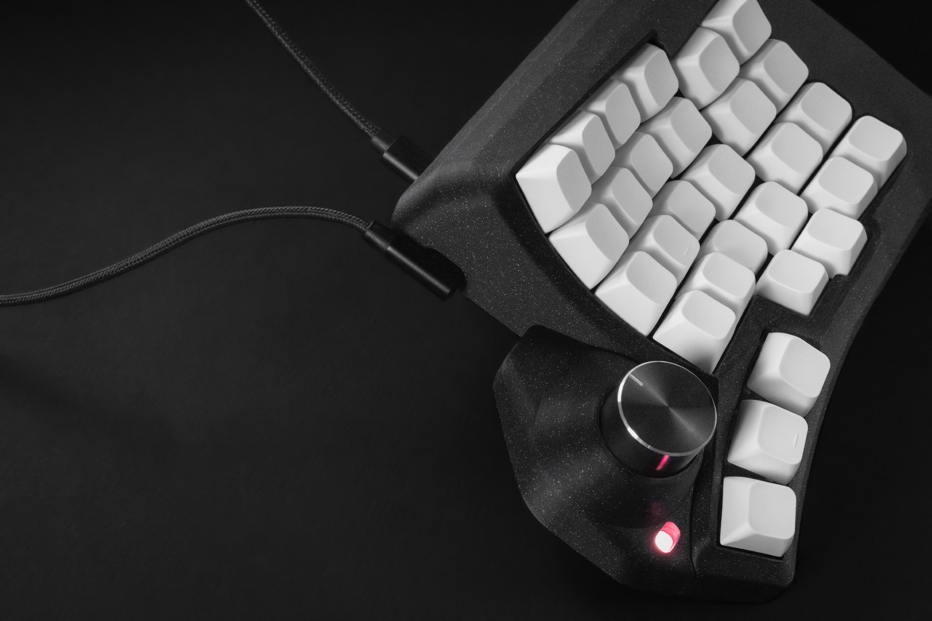 Close-up of a Phenom keyboard half with white keycaps, rotary encoder, and connected cables